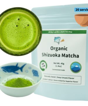 Product photograph featuring Organic Shizuoka Matcha tea showcased in three different forms. The image displays a circular arrangement with the prepared beverage, dry powder, and packaging. On the left side, a dark ceramic bowl contains bright vibrant green matcha tea with a frothy surface displaying small bubbles, demonstrating the traditional whisked preparation. Below it, a small porcelain dish with blue fish and marine motifs contains fine, vivid green matcha powder in its dry form. On the right, a light blue resealable pouch features the product name 'Organic Shizuoka Matcha' prominently displayed on a white label. The package indicates '20 servings' in a blue label at the top corner, with a small illustration of a clay tea bowl. Product details include 'Net Wt. 40g (1.4oz)' and 'Ceremonial Grade' designation. The packaging includes a circular logo featuring a stylized Mt. Fuji with blue water and sky. Descriptive text reads 'Naturally Sweet | Deep Umami Flavor' and 'Premium Cultivar | Stone-milled for Superior Flavor.' A green banner across the top of the label displays the brand's cartoon shark logo with text 'all day i eat like a shark | tea shop.' The composition effectively shows the product's organic certification, premium quality, and traditional Japanese origins, while demonstrating both its powdered form and prepared appearance.